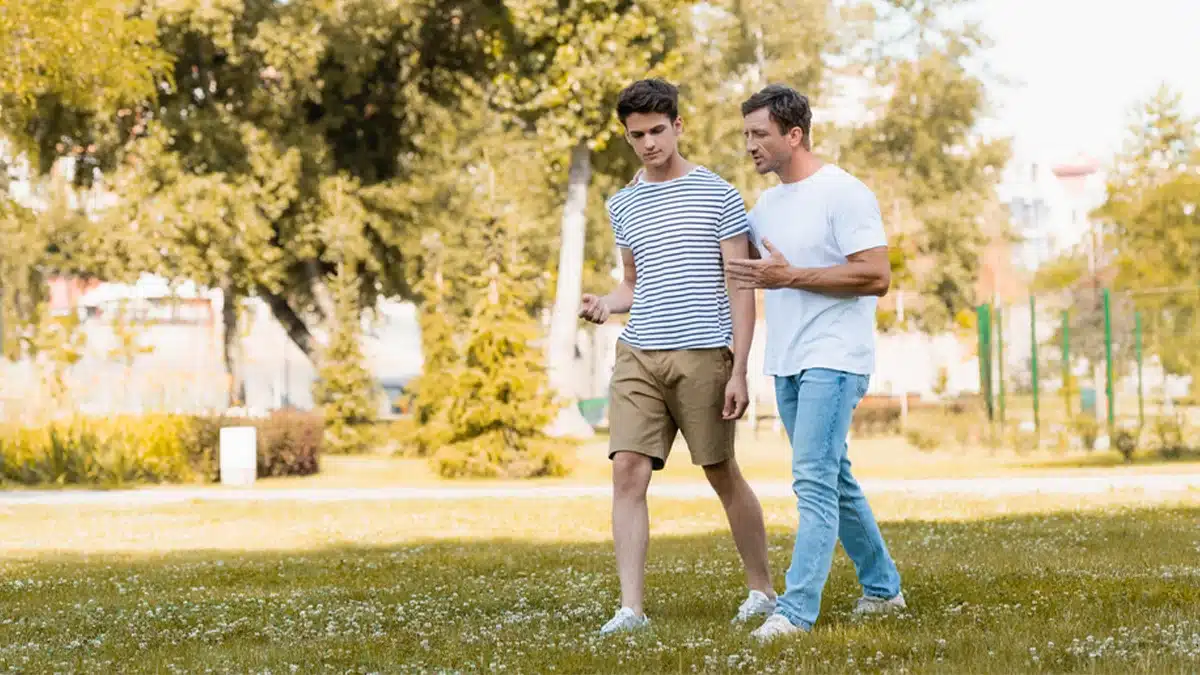 Man walking in a park with his teenage son. When explaining addiction to your child, use age-appropriate language to help them understand