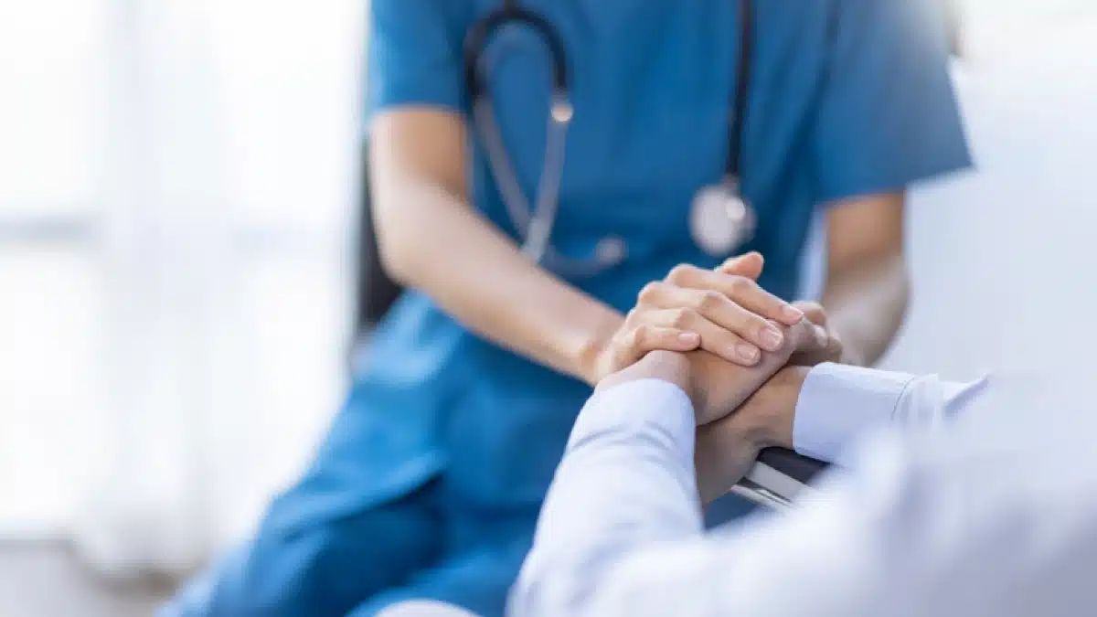 Nurse with a stethoscope holds a patient’s hands.