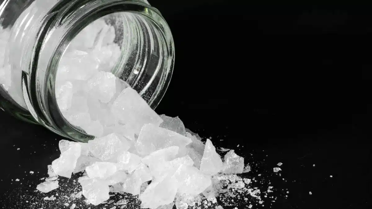 White crystal substance spilling out of a clear jar. Blue text on a green background explains factors that influence amphetamine metabolism. White crystal substance spilling out of a clear jar.