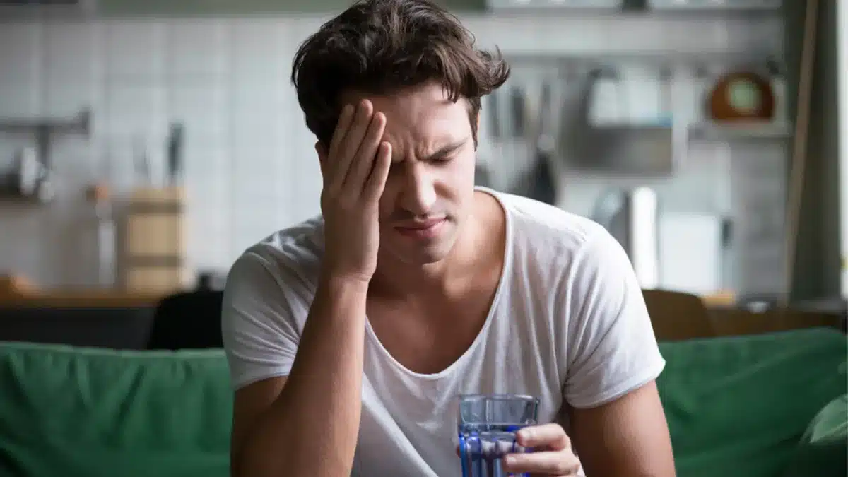 Teen boy holding his head and a glass of water.