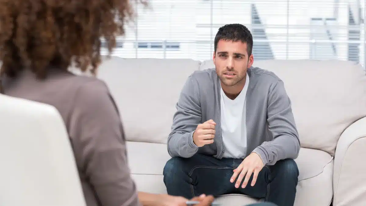 man sitting on a couch in a well lit room speaking to a therapist