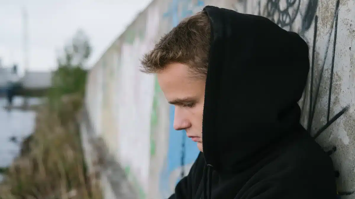 teenager with a hoodie resting his back on a wall outside