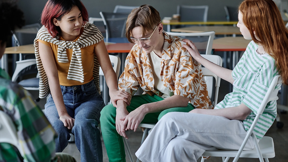 teenager being consoled by a woman in a group therapy session