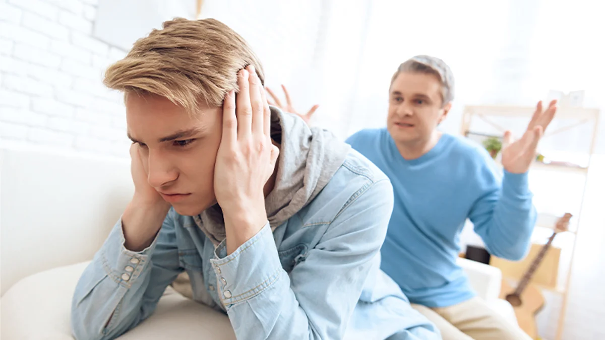 Teen with his hands on his ears as his father berates him