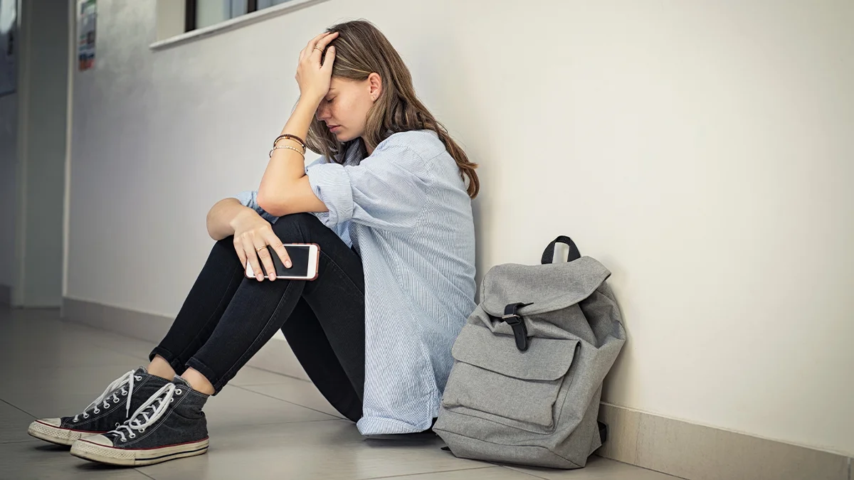 Disgruntled teen sitting with her back on the wall and her backpack besides her