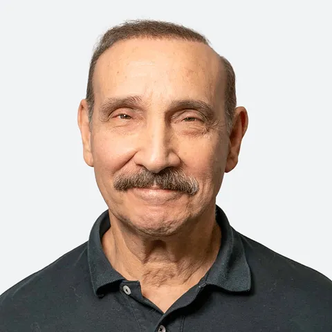 Professional headshot of an older man with short brown hair and a mustache, wearing a dark polo shirt and smiling against a light gray background.