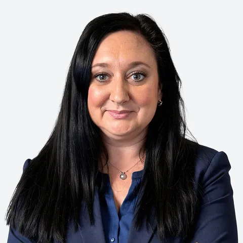 Professional headshot of a woman with long black hair wearing a navy blazer and blue blouse, smiling against a light background.