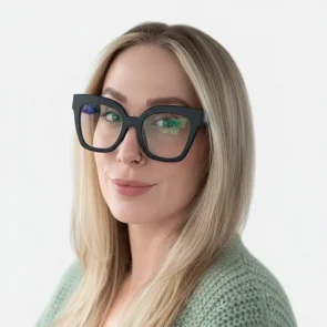 A woman with long blonde hair and black-framed glasses smiles softly at the camera. She is wearing a light green knit sweater and has a nose ring, with a clean white background behind her.
